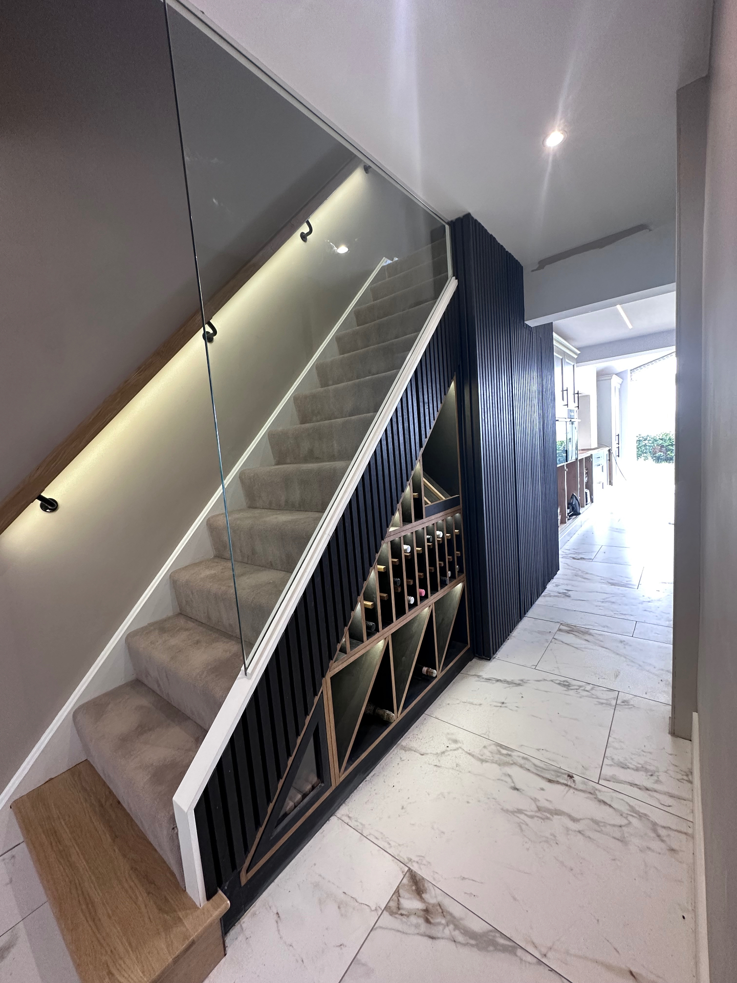 Remodelled staircase with frameless glass balustrade, oak handrail, panelled side and lit understairs wine store